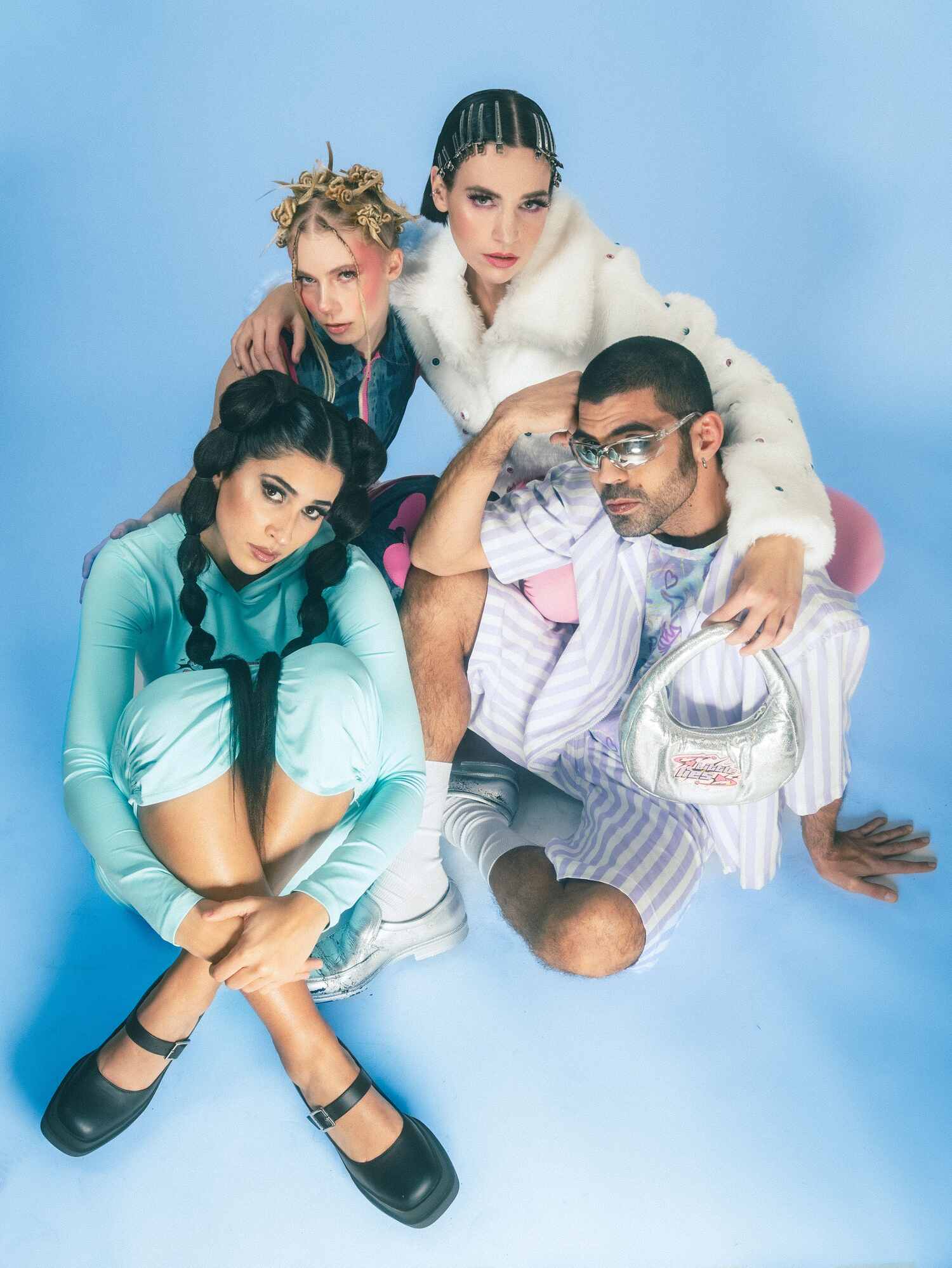 Group of four models styled in playful, pastel-toned outfits with bold accessories, posing against a soft blue backdrop for Sunday Morning’s “Little Lies” collection.