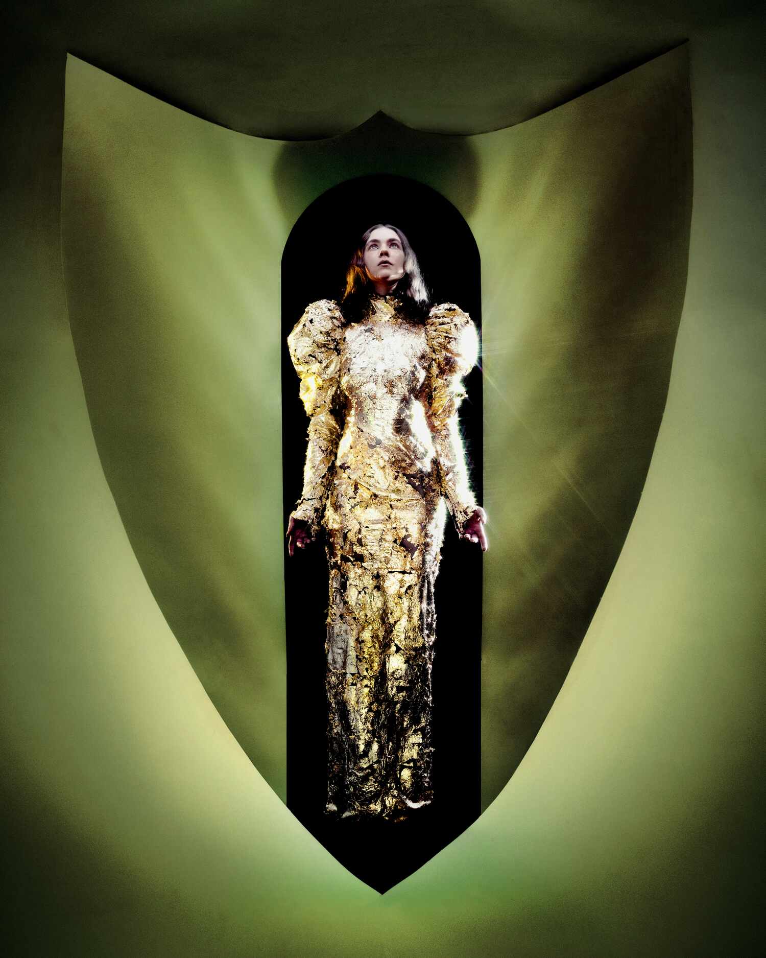 Model in shimmering gold gown with puffed sleeves from Elodie Carstensen’s AW25 collection, lit inside a shield-shaped arch.